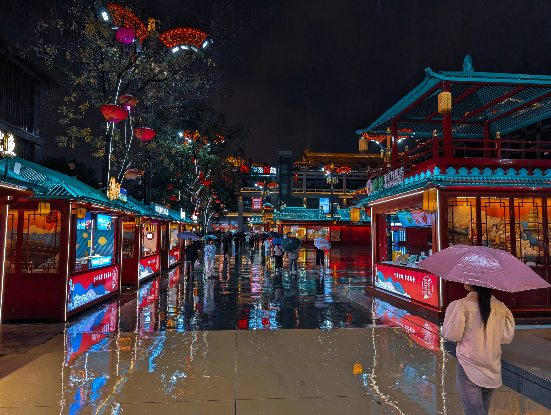 A visitor with an umbrella on a rain-soaked street beneath colourful lanterns