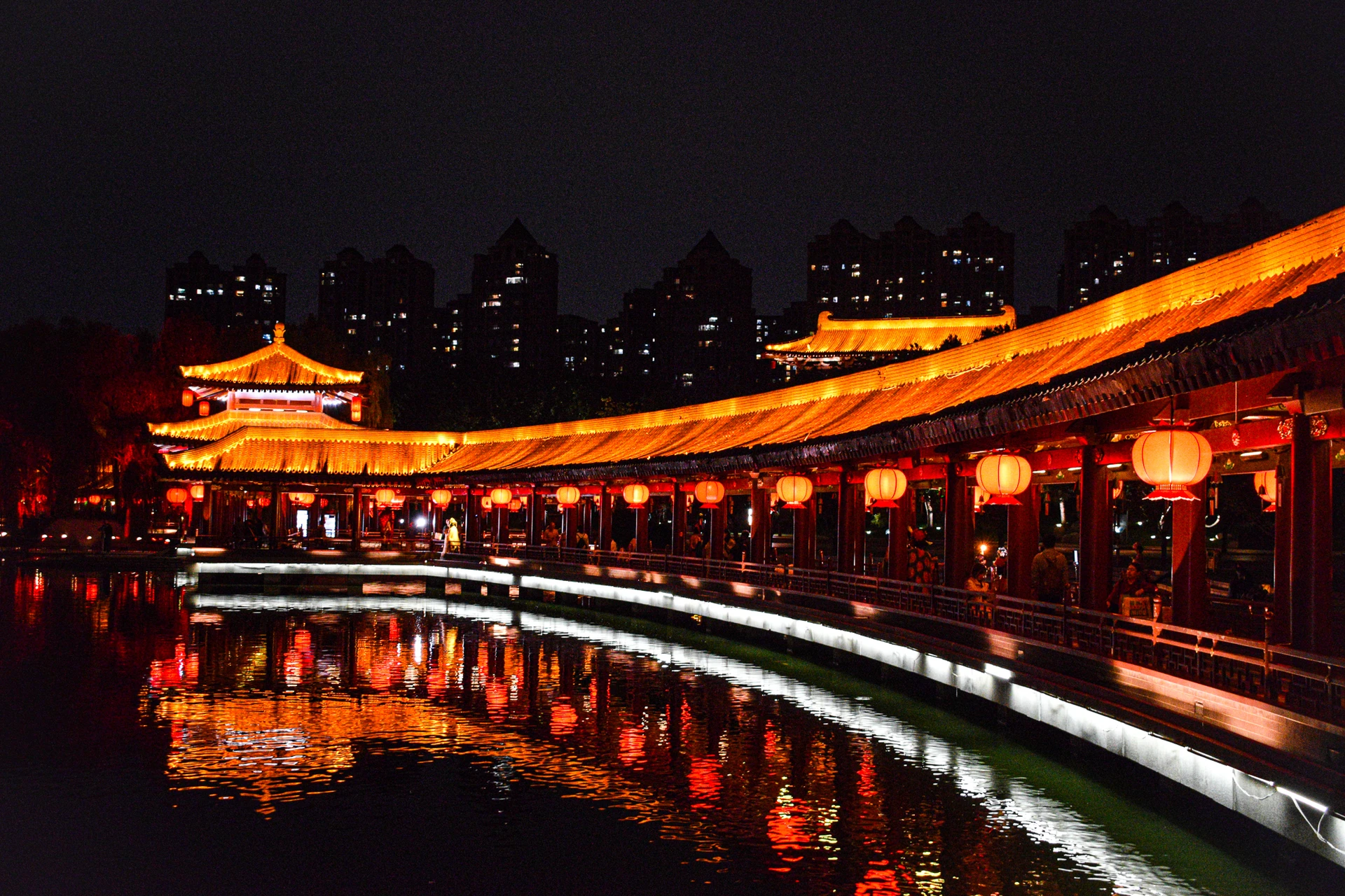 A covered bridge glowing with red lanterns and reflected in the water