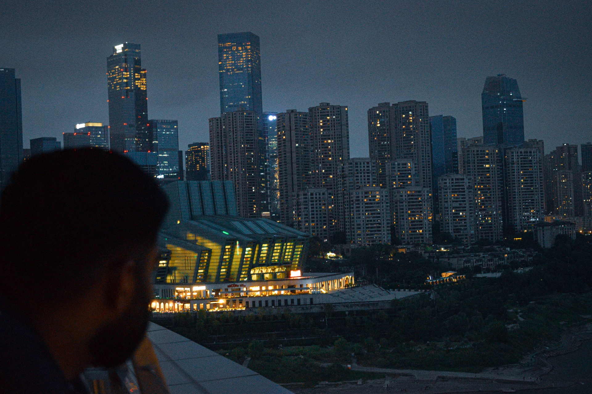 A silhouetted visitor looking towards a riverside skyline at dusk