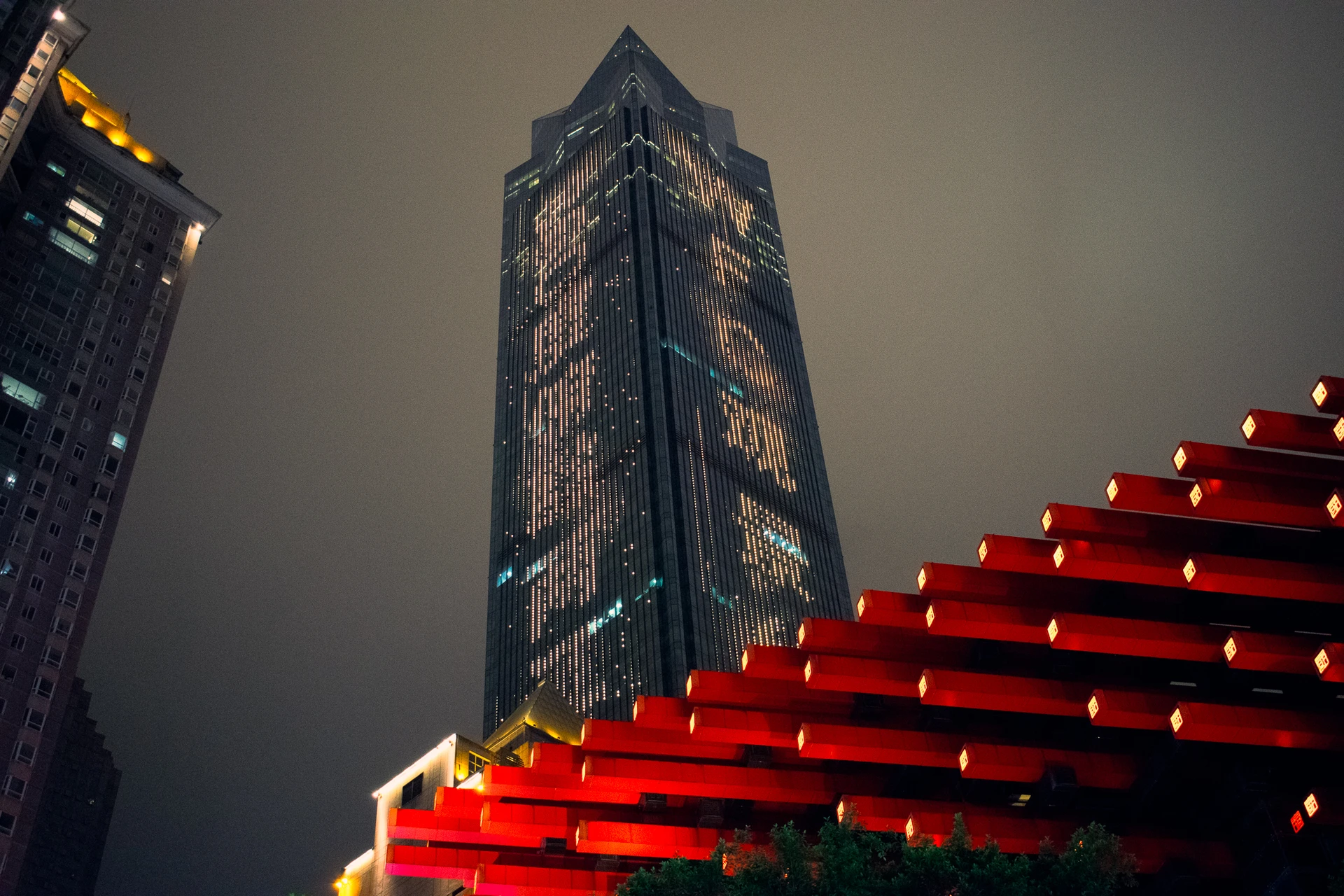 A skyscraper rising above rows of glowing red lanterns
