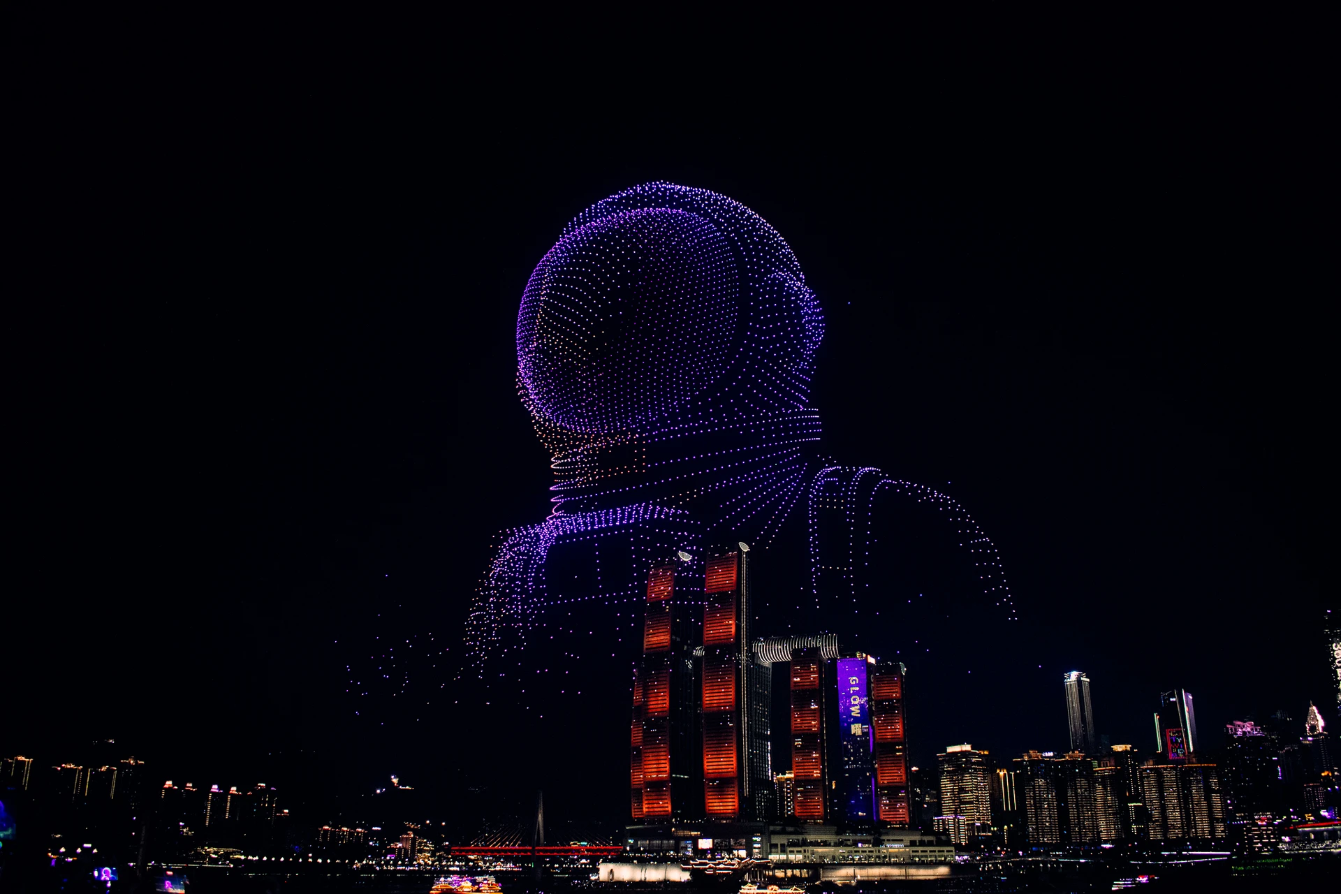 A purple figure formed by a drone light display above the city at night