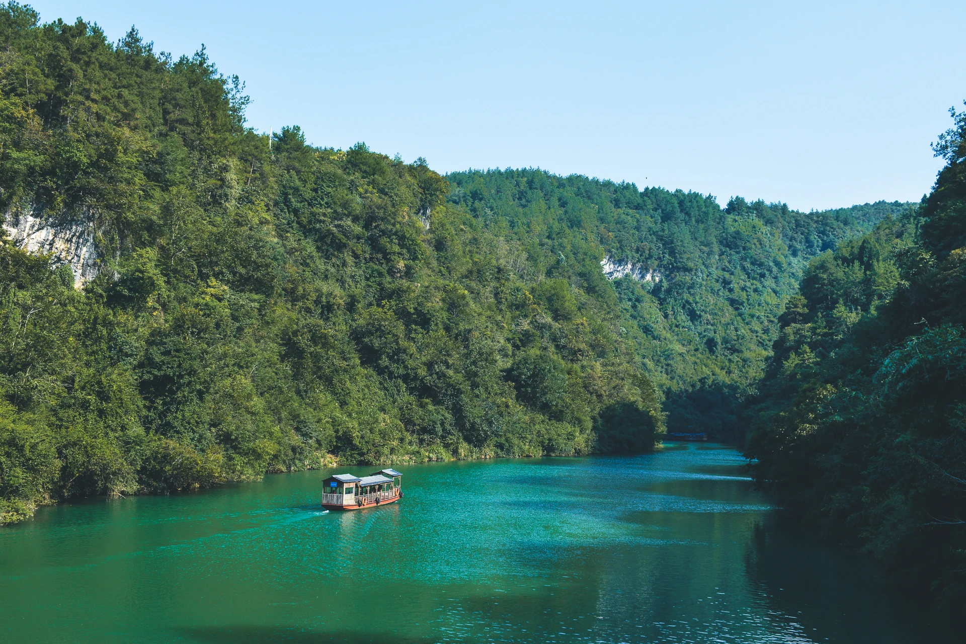A small boat on a turquoise lake surrounded by forested cliffs