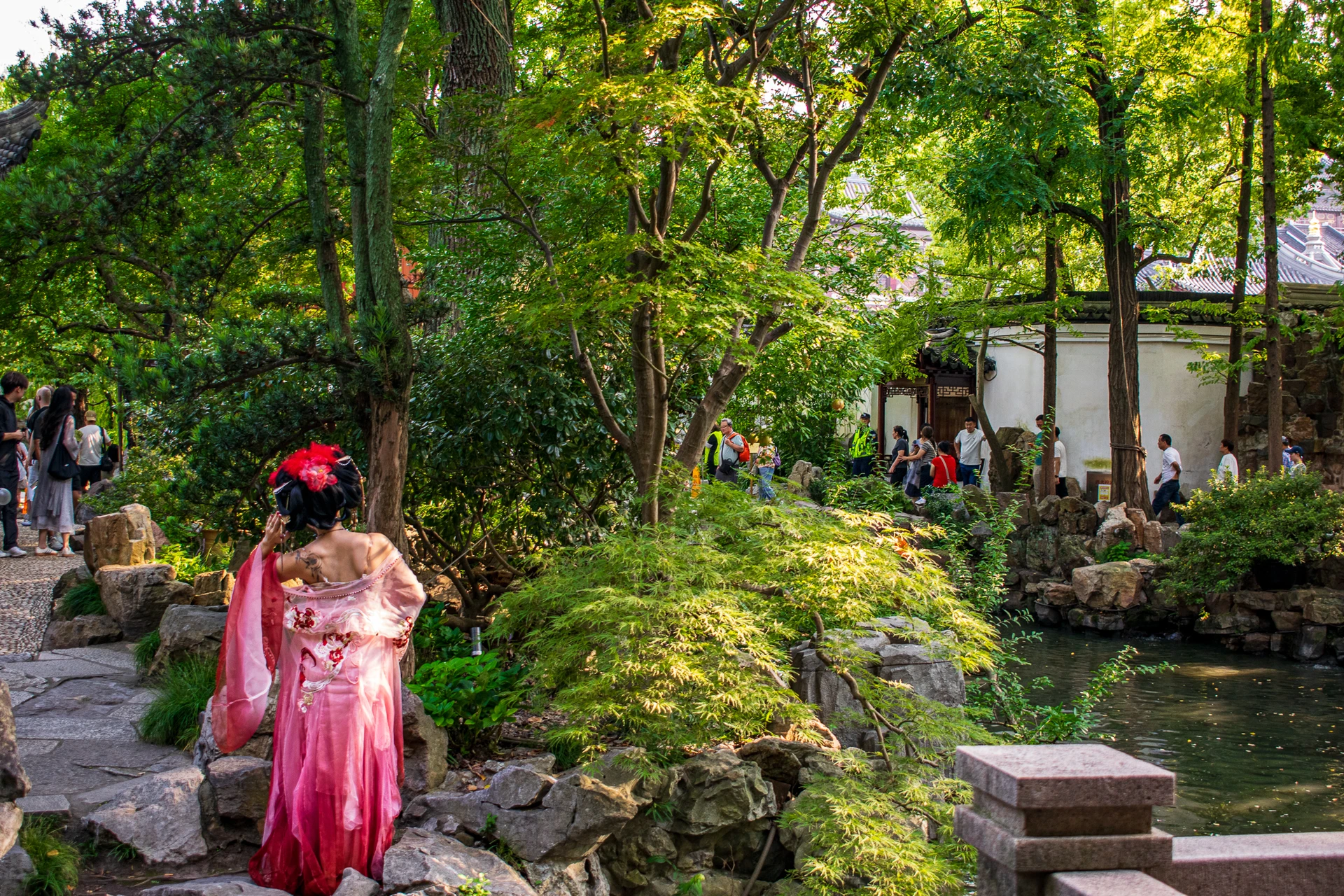 A visitor in a pink dress walking through a leafy garden with rocks and winding paths