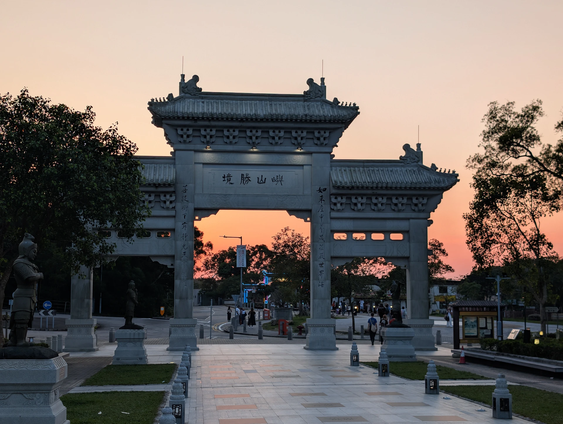 An ornate stone gateway framed by trees against a peach-coloured evening sky